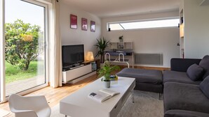 Ein modernes Wohnzimmer mit Flachbildfernseher, Esstisch, Sofa und einer großen Glasschiebetür, die zu einem Garten führt.