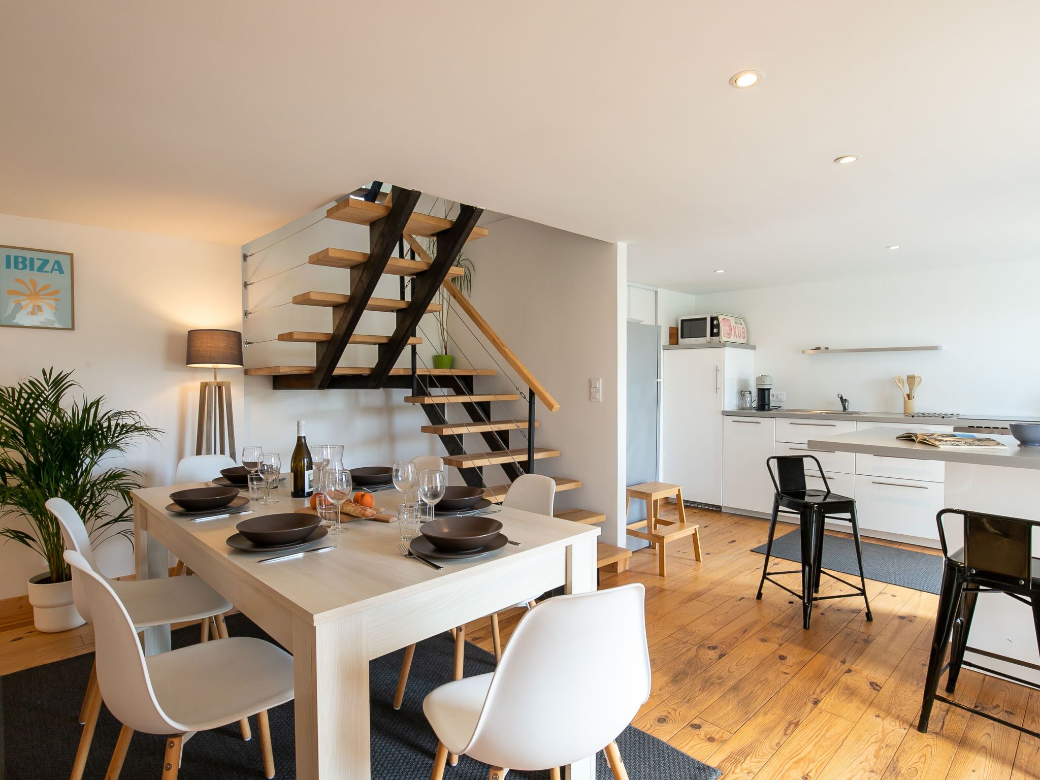 A modern apartment with a dining area, kitchen, and a wooden staircase.