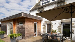 Ein modernes Haus mit einer Holzdiele, einem Essbereich mit Gartenmöbeln und einer Steinmauer.