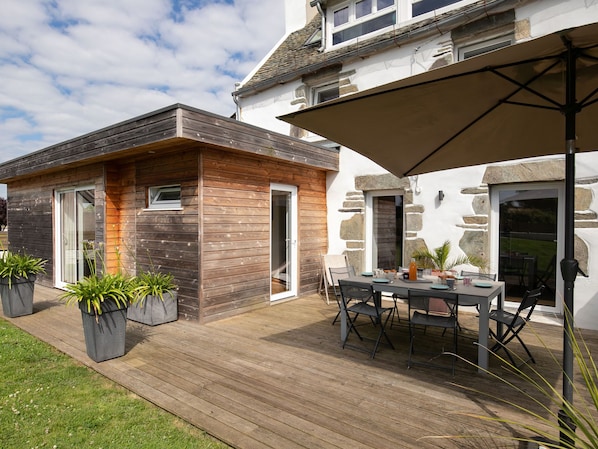 A modern house with a wooden deck, a dining area with outdoor furniture, and a stone wall.