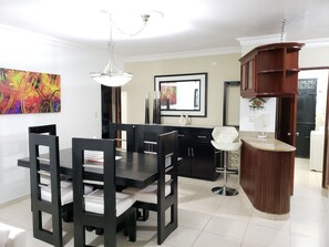 Un comedor moderno con una mesa y sillas negras, una lámpara colgante blanca y un aparador de madera.