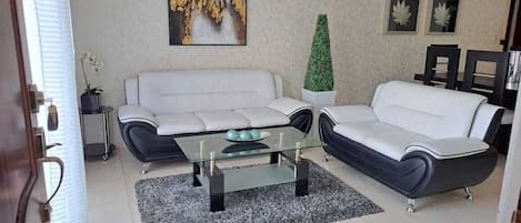 A living room with a white sofa, a black sofa, a glass coffee table, and a green topiary.