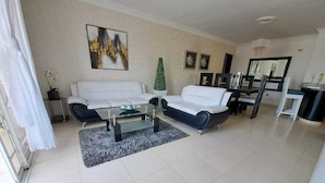 A spacious living room with two white sofas, a glass coffee table, and a small green plant. - Próximo a unión medica 2 hab. (Santiago de los Caballeros)