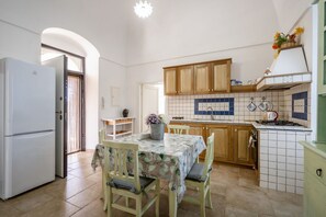 A kitchen with a refrigerator, wooden cabinets, a tiled backsplash, and a dining table with chairs.