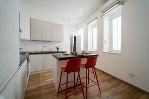 Une cuisine moderne dotée d’un îlot central, de deux tabourets de bar rouges et d’une fenêtre laissant entrer la lumière naturelle.