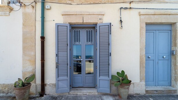 A building entrance with a blue door, two potted plants, and a number '50' on the wall.
