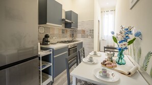 Una cocina compacta con electrodomésticos modernos, un comedor con una mesa dispuesta para dos personas, y un jarrón decorativo con flores.