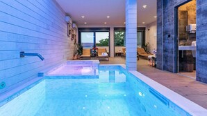 En modern inomhuspool med fri sikt över det omgivande loungeområdet, inklusive sittplatser och utsikt mot utomhusmiljön.