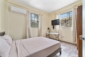 A bedroom with a bed, a desk, a TV, and an air conditioning unit. - Home at Dr Grooms Beach Road (St. George's)