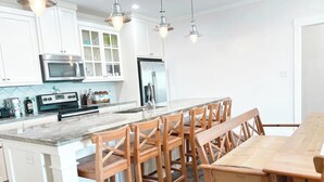 A modern kitchen with white cabinets, stainless steel appliances, and wooden bar stools. - Elegant home 180 steps from the Beach, 2 King beds, Arcade (Bolivar Peninsula)