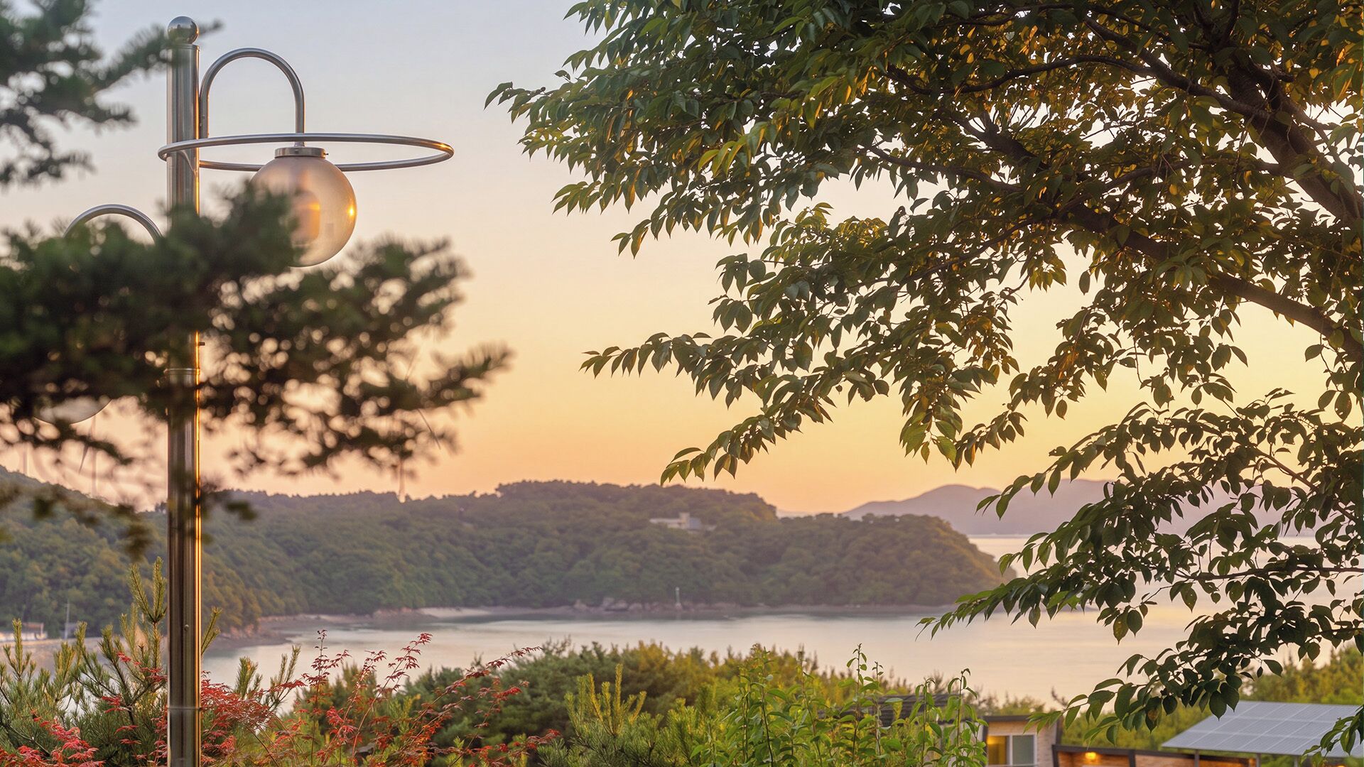 A scenic view of a lake with a sunset, a lamp post, and a building with solar panels.