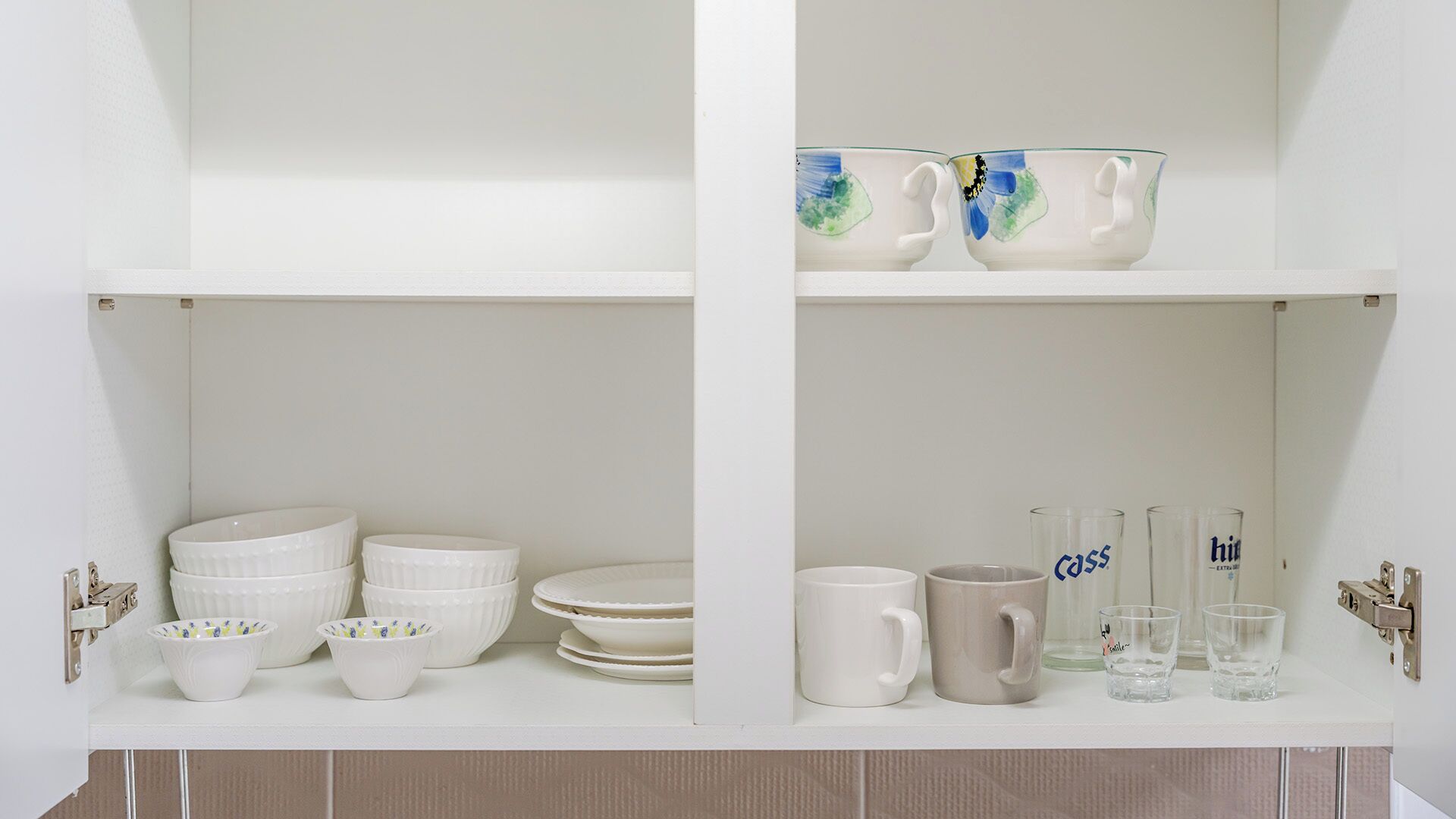 A white shelf with white bowls, plates, and a mug.