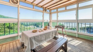 A conservatory with a table set for dining, a wooden bench, and a view of a green landscape.