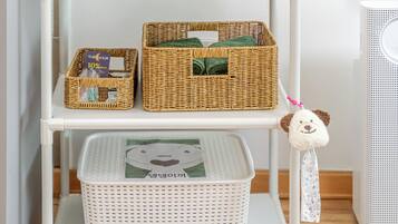 A white shelf with three wicker baskets and a white plastic bin with a cartoon character.