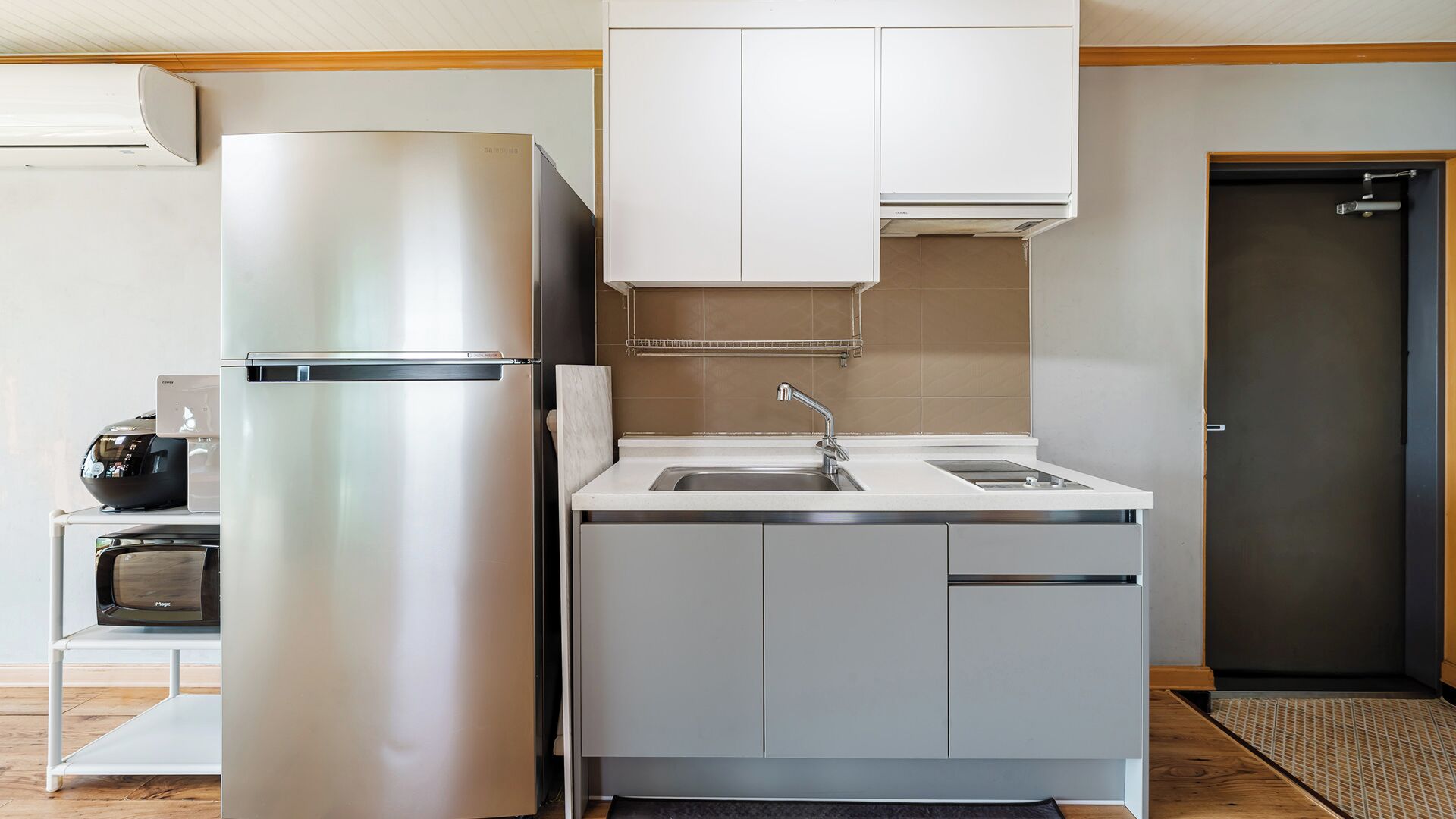 A compact kitchen with a stainless steel refrigerator, a built-in sink, and a microwave.
