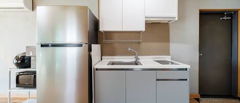 A compact kitchen with a stainless steel refrigerator, a built-in sink, and a microwave.
