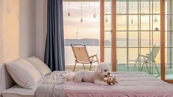 A bedroom with a bed, a chair, and a view of the sea.