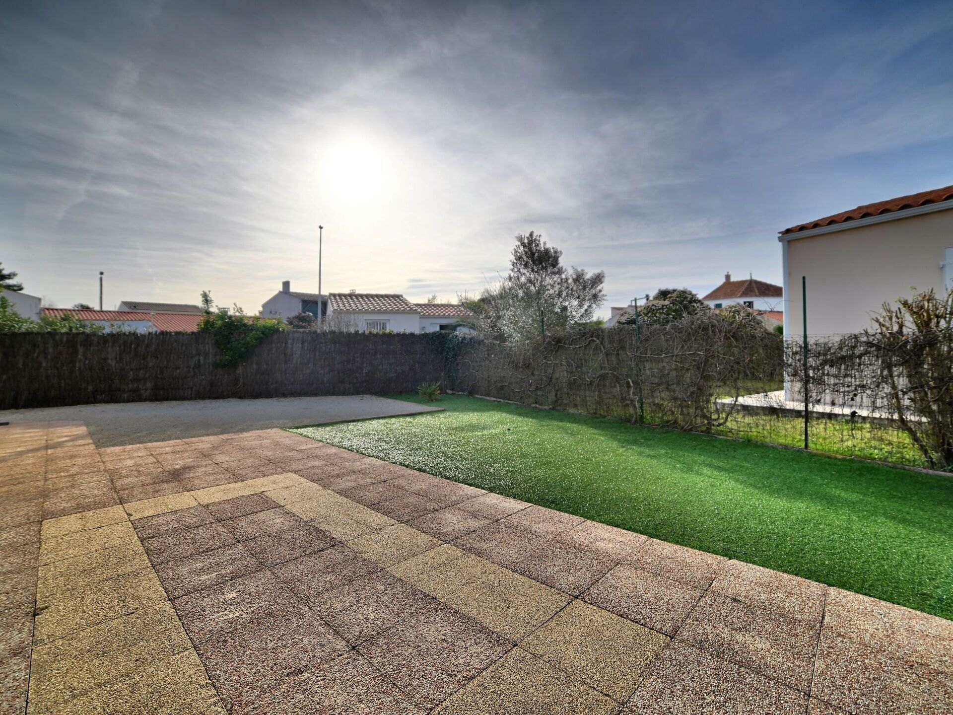 A residential backyard with a paved patio area, a well-maintained lawn, and a stone wall.