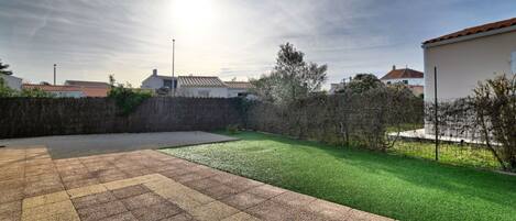 A residential backyard with a paved patio area, a well-maintained lawn, and a stone wall.