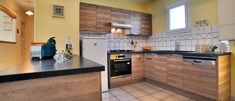 Een moderne keuken met houten kastjes, een zwart aanrecht en een betegelde vloer.