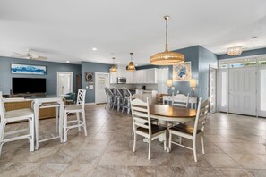 Un vaste espace de vie comprenant une table à manger, des chaises, un téléviseur et une cuisine en arrière-plan.