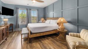 Quarto com cama, luminárias de cabeceira, televisão, escrivaninha de madeira e janela com cortinas.
