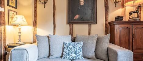 Un saló d'estar acollidor amb un sofà gris, un coixí decoratiu amb dibuixos, panells de paret de fusta, un retrat emmarcat i un moble de fusta.