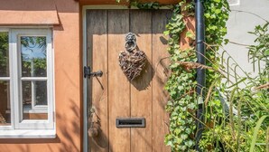 Une porte en bois ornée d’un décor en forme de cœur, une fenêtre à cadre blanc et de la verdure qui pousse sur le mur.