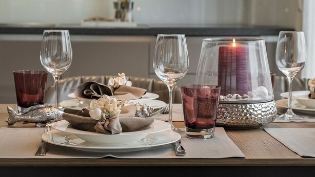 Mesa de jantar posta com pratos, copos e uma vela.