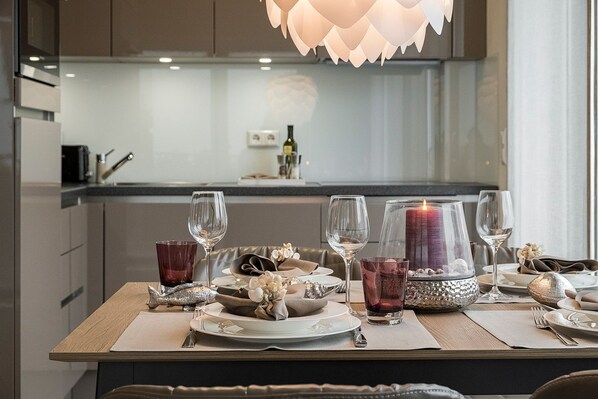 A modern dining area with a wooden table set for four, featuring clear glassware and a candle centerpiece. - Haus Möwenberg 15 - Haus Möwenberg 15 Appartement 04 (Scharbeutz)