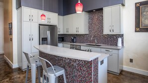 A modern kitchen with white cabinets, a stainless steel refrigerator, a microwave, and a tiled backsplash. - Sta-Haus | Wonderful Location (Fredericksburg)