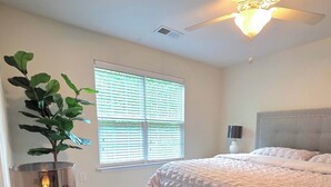 Une chambre à coucher avec un lit, un ventilateur de plafond, une fenêtre avec des stores et deux bougies posées sur une table.