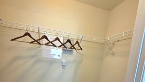 Une petite pièce, recouverte de moquette, avec une porte blanche, une étagère en métal avec des cintres en bois et un panier à linge.