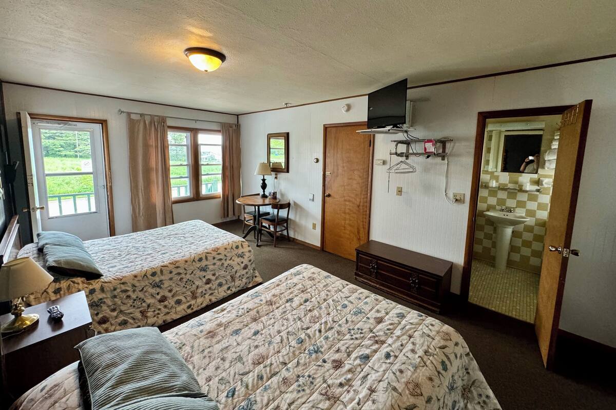 A hotel room with two beds, a desk, a chair, a television, a mirror, and a bathroom visible through an open door.