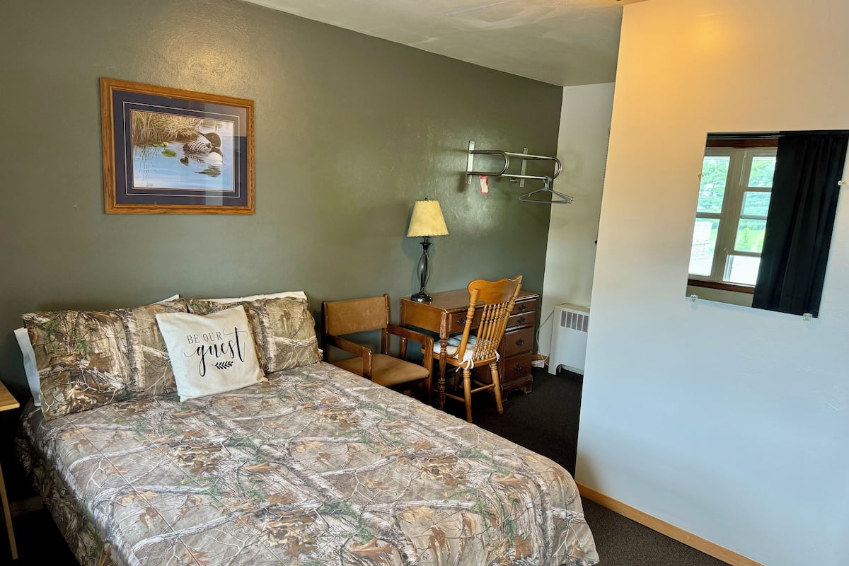 A bedroom with a bed, a chair, a dresser, a lamp, and a window.
