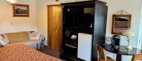 A bedroom with a bed, a desk with a chair, a wardrobe, a television, and a refrigerator.