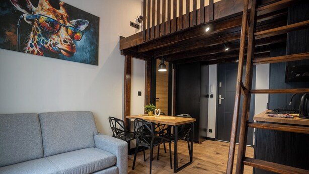 Ein modernes Wohnzimmer mit einem grauen Sofa, einem Holzesstisch mit Stühlen und einem Giraffenbild an der Wand.