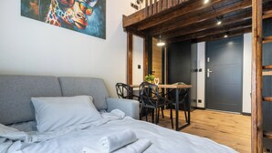 Ein Schlafzimmer mit einem Bett, einem grauen Sofa, einem Esstisch mit Stühlen und einem Gemälde an der Wand.