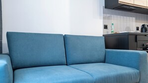 A blue sofa in a modern kitchen with white tiles and a black countertop. - Żwirki i Wigury Apartment #2 (Katowice)