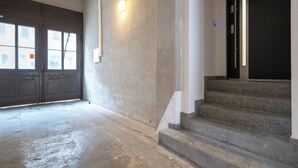 A staircase leading to a dark door, a light switch on the wall, and a garage door. - Żwirki i Wigury Apartment #2 (Katowice)