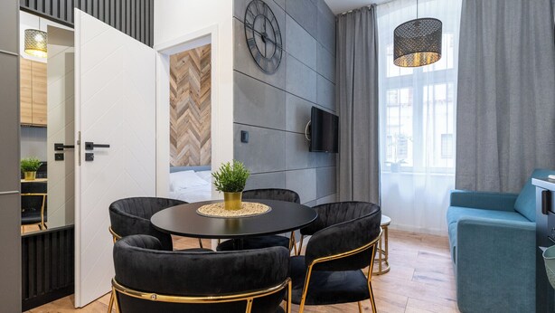 A modern living room with a round table, black velvet chairs, a blue sofa, and a large window with curtains. - Żwirki i Wigury Apartment #2 (Katowice)