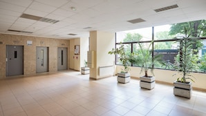 A spacious lobby with a tiled floor, three elevators, and potted plants. - Rondo ONZ Standard Studio (Warszawa)
