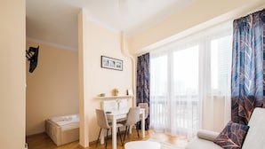 A cozy living room with a sofa, a dining table with chairs, a small white table, and a radiator. - Rondo ONZ Standard Studio (Warszawa)