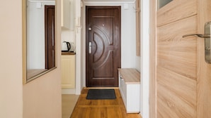A hallway with a wooden door, a bench, and a kitchen area with a kettle. - Rondo ONZ Standard Studio (Warszawa)