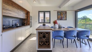 Een moderne keuken met een inbouw eiland, een eetgedeelte met blauwe stoelen, en een groot raam met uitzicht op groen.