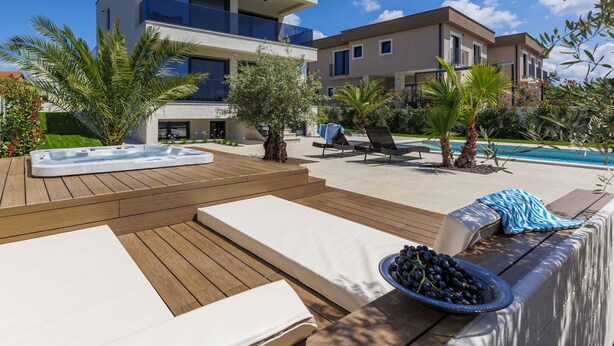 Een modern buitenzwembad met ligbedden, een jacuzzi en een houten terras.