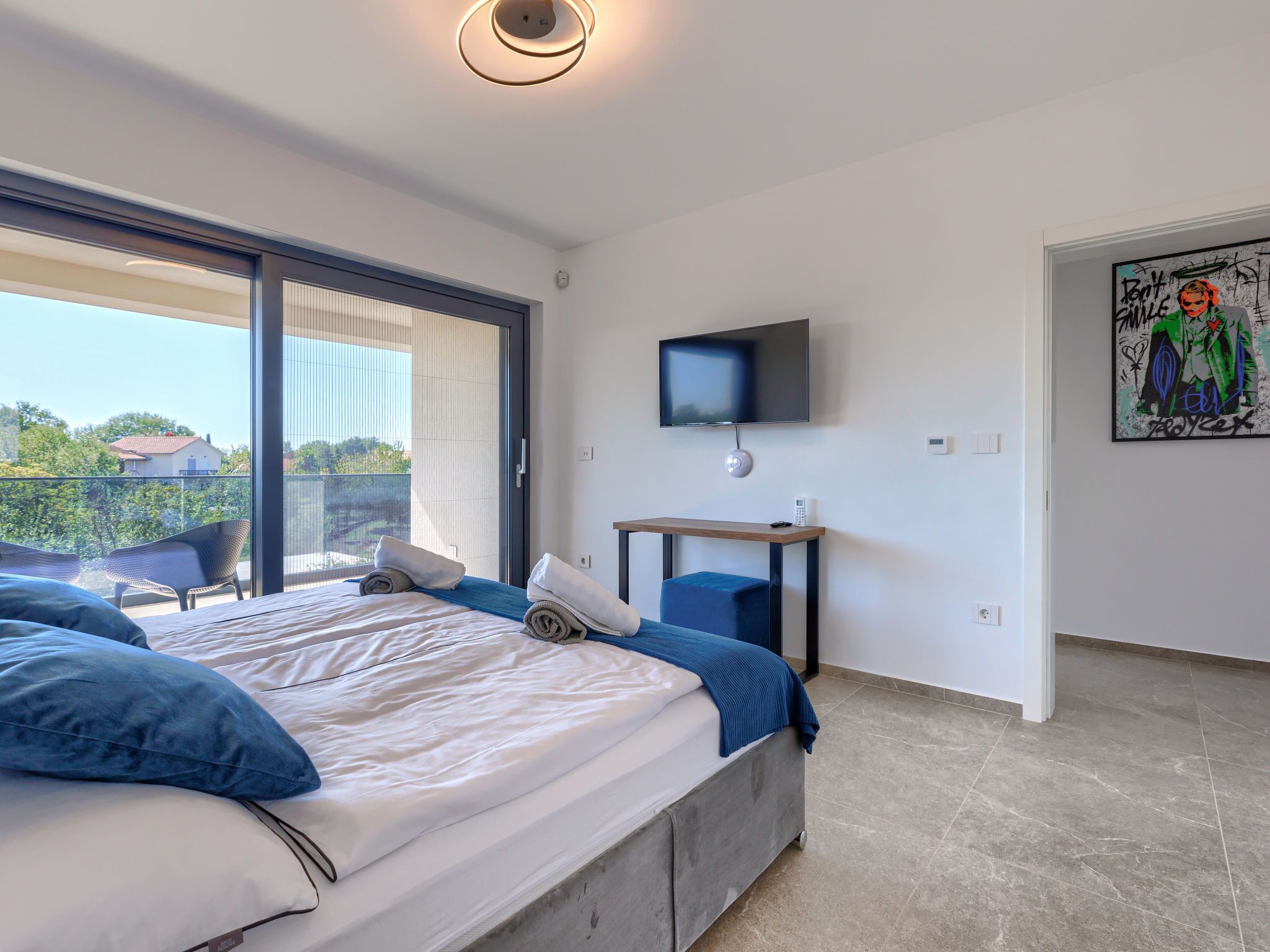 Ein modernes Hotelzimmer mit einem großen Bett, einem Schreibtisch, einem Flachbildfernseher und einem Balkon mit Sitzgelegenheiten.