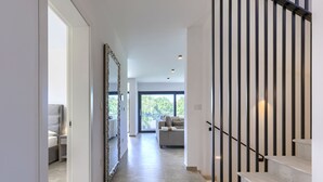Een modern interieur met een trap, een gang naar een woonruimte en een groot raam dat natuurlijk licht binnenlaat.