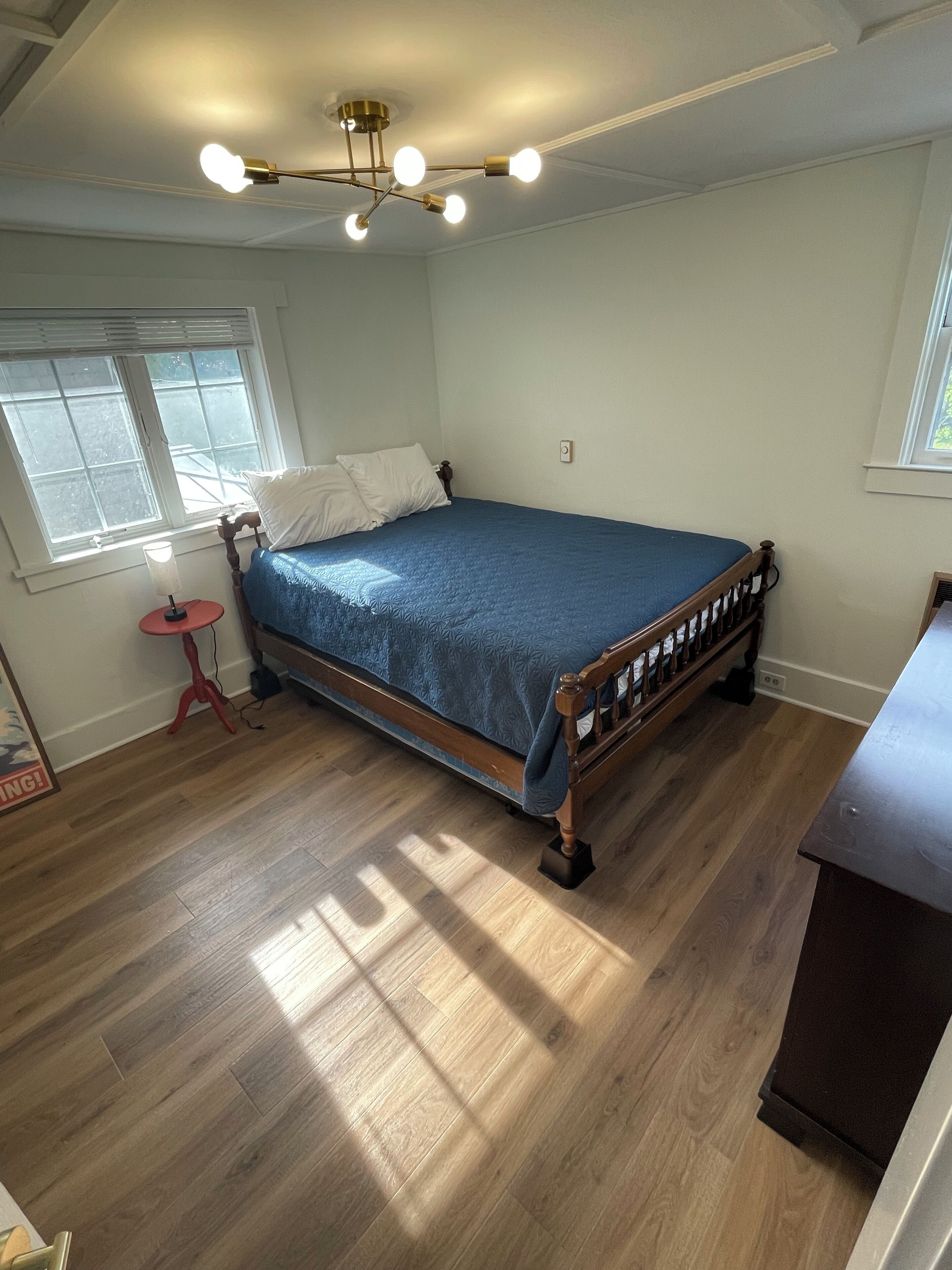 Une chambre à coucher avec un lit en bois, une petite table de chevet, une lampe rouge et une fenêtre avec des stores.