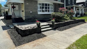 A two-story house with a front porch, a stone pathway, and a well-maintained garden.